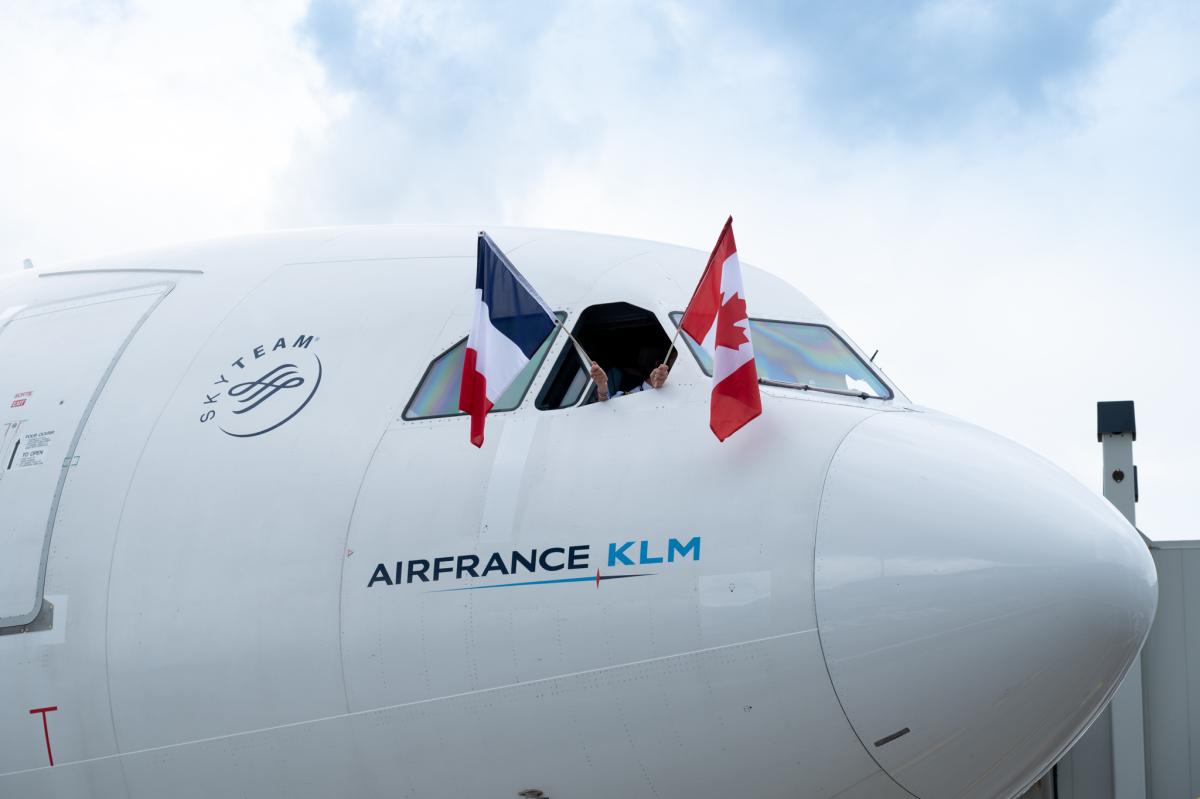 Aircraft nose branded with Air France KLM, pilot's window open two hands sticking out holding a France flag and a Canada flag. Aircraft nose branded with Air France KLM, pilot's window open two hands sticking out holding a France flag and a Canada flag
