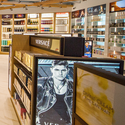 Versace ad of man standing with a leather coat mounted on a display of Versace perfume in front of shelves with liquor bottles